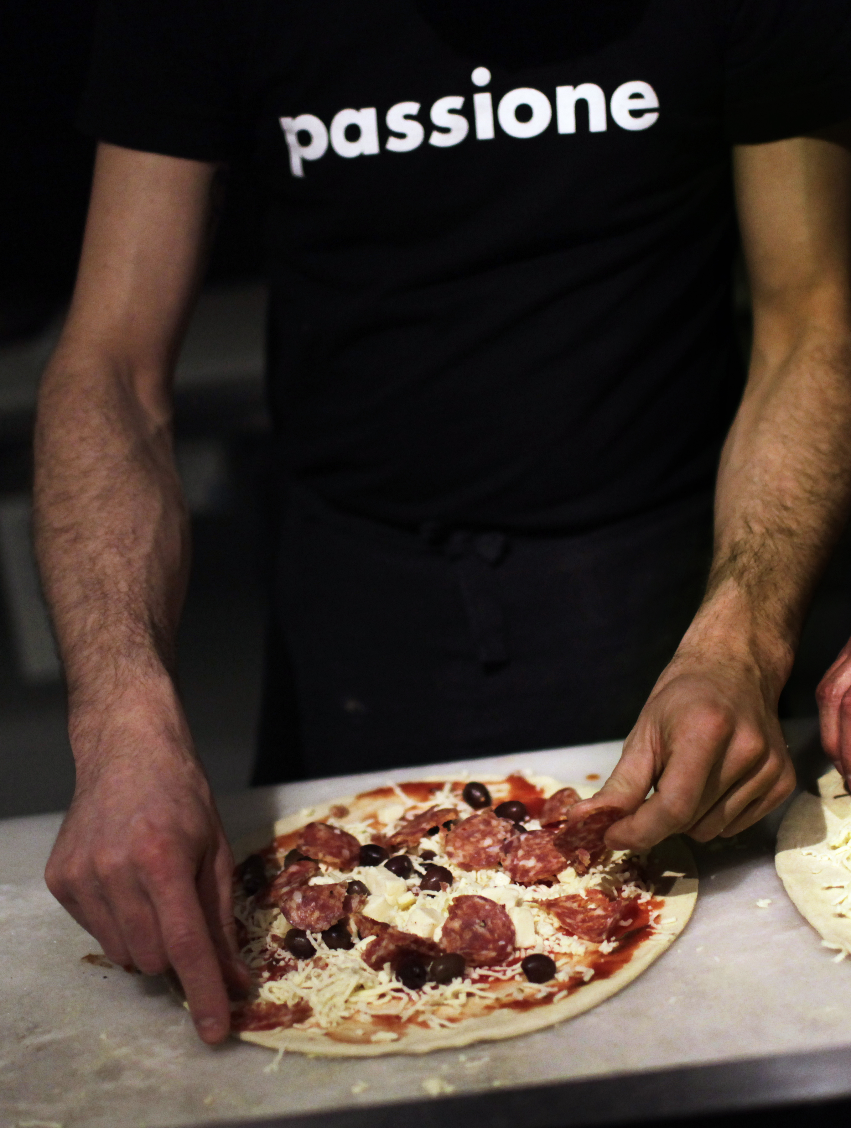 Topping a pizza with salami and olives in the Passione kitchen
