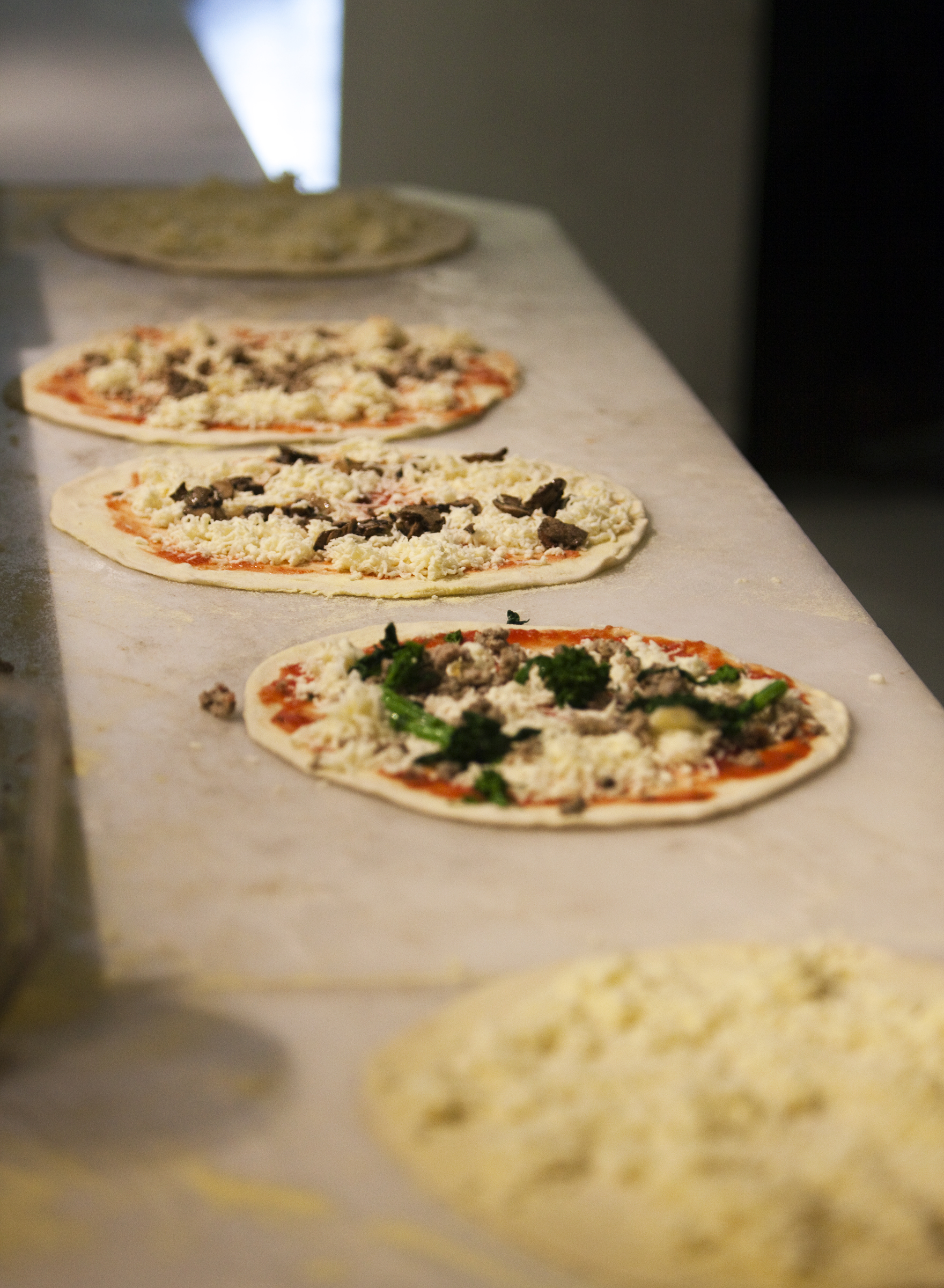 Topped pizzas lined up on the marble bench